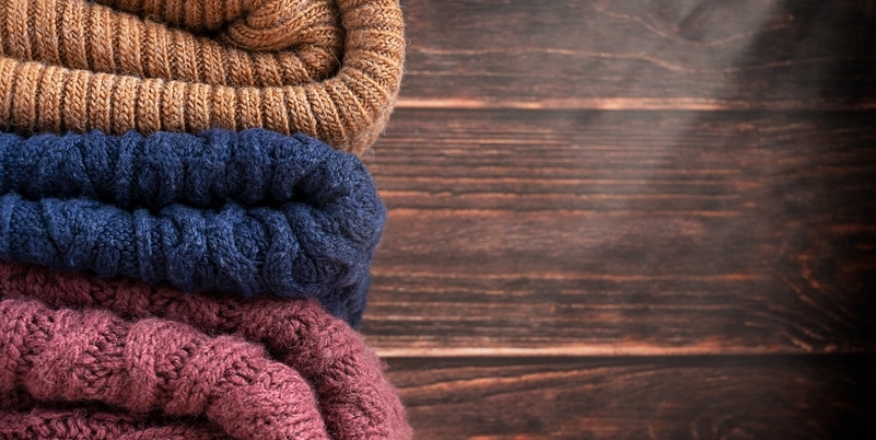 Maglioni di lana piegati in diversi colori su sfondo in legno scuro.