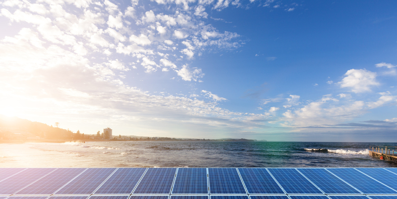Vista sul mare con pannelli solari in primo piano, rappresentazione simbolica della produzione di energia pulita da fonti rinnovabili come sole, vento e onde nel progetto NoviOcean.